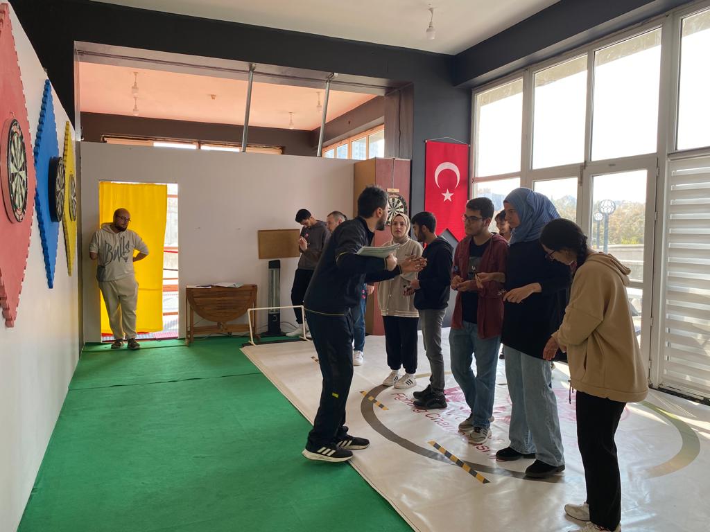 Dart konusunda bilgilendirme yapılırken, iki kişi dart oynarken, etkinlik sonrası toplu fotoğraf çekiminden kareler