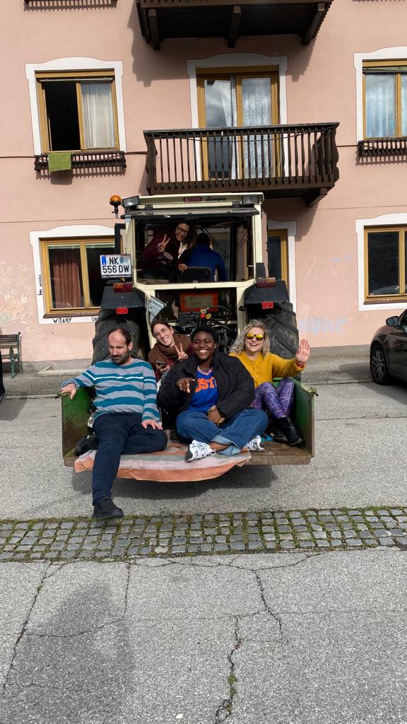 Birkaç katılımcı traktör arkasına yerleştirilmiş bir taş üzerinde oturmakta.