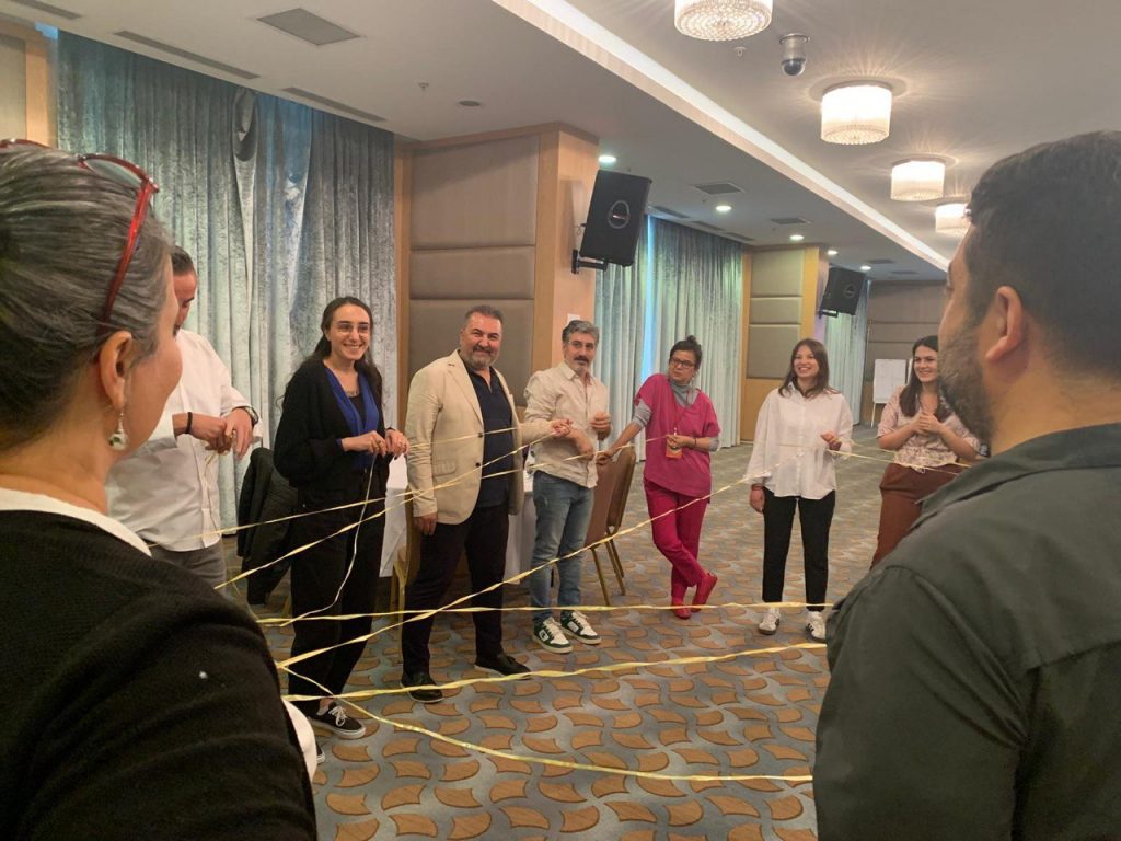 Örümcek ağı metaforuyla bir ip ile oyun oluşturmuş 20 kişi ayaktadır