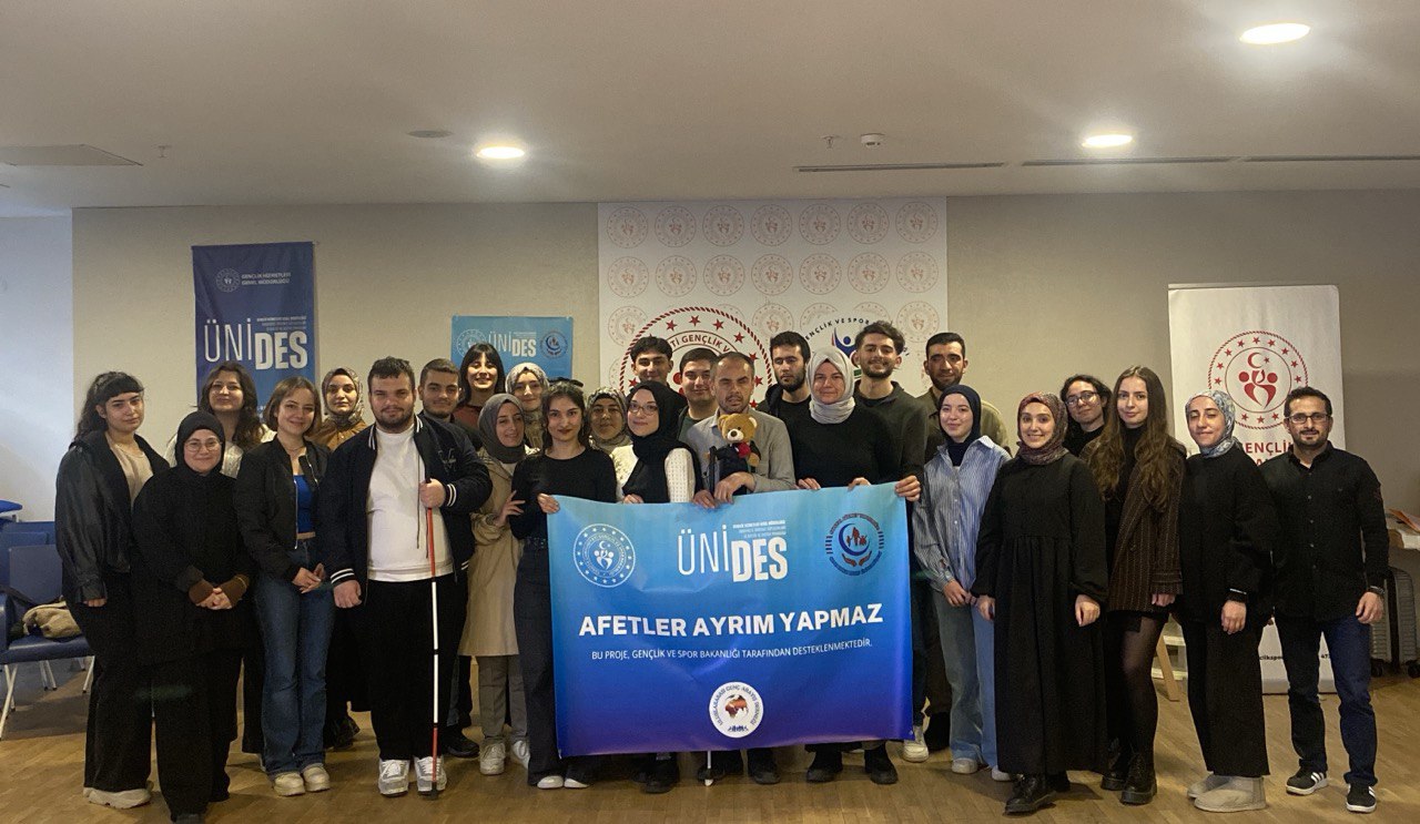 elinde afetler ayrım yapmaz yazılı pankart tutan 25 kişi ayakta bir arada poz veriyoe